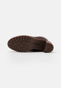 Sole hnědé Timberland boty s hlubokým vzorem podrážky, včetně gripů a květinových vzorů na bílém pozadí.