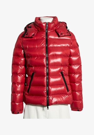 Chaqueta acolchada roja brillante con cremallera negra y bolsillos con cremallera, cuello alto y puños abotonados en un torso de maniquí blanco.
