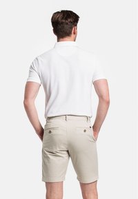 Witte polo met korte mouwen gecombineerd met beige shorts. De shorts hebben twee achterzakken met bruine knopen en een opgerolde zoom.