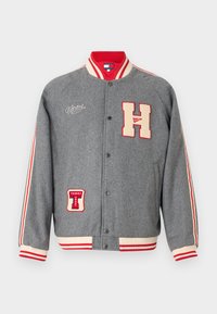 Szara kurtka varsity z czerwonymi i kremowymi akcentami, z haftowanymi łatami 'H' i 'TOMMY JEANS'. Rybaczka z prążkowanym kołnierzem i mankietami. Zapięcie na zatrzask.