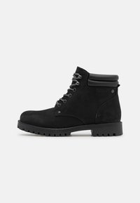Stivaletti neri in suede alla caviglia con punta arrotondata, suola in gomma nera e lacci grigi. Presentano un colletto imbottito per un maggiore comfort.