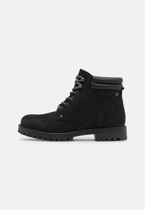 Bottines en suède noir avec un bout rond, semelle en caoutchouc noir et lacets gris. Elles sont dotées d'un col rembourré pour un confort supplémentaire.