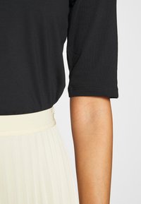 Top nero a maniche corte con scollatura rotonda, abbinato a una gonna plissettata color crema con una ampia vita elastica.