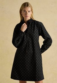 Melns kleita, kas izgatavota no auduma ar pogu priekšpusi un garām piedurknēm. Iezīmēts ar izkaisītu ziedu rakstu zelta toņos.