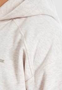 Felpa beige chiaro realizzata in un tessuto morbido e testurizzato. Presenta un cappuccio con cordino e un sottile dettaglio del logo sul lato.
