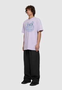 Fialové oversized tričko s modrou grafikou znázorňující číslo "29" a hvězdy, v kombinaci s volnými černými kalhotami a černými teniskami.