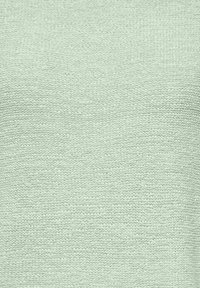 Tissu tricoté vert clair avec une texture douce, présentant un motif simple et un tissage uniforme, adapté aux vêtements ou accessoires.