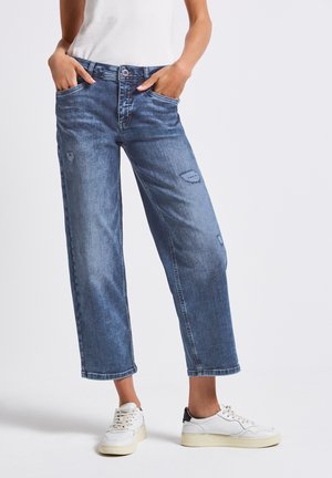 Light blue denim jeans with a relaxed fit, featuring front pockets, distressed detailing, and rolled hems, paired with white sneakers.