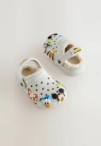 Des sabots en mousse blanche ornés de motifs colorés de personnages Disney, avec une doublure intérieure douce, des trous de ventilation et une sangle arrière pour un bon maintien.