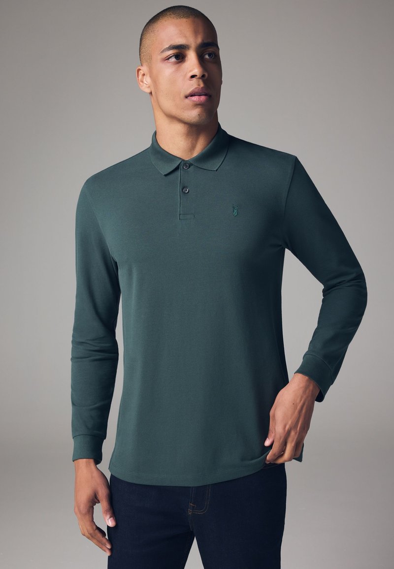 Langærmet polo shirt i mørkegrøn stof, med krave, tre knapstolper og et lille logo på venstre bryst.
