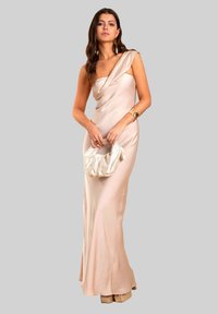 Robe de soirée en satin couleur beige clair avec un design drapé à une épaule. Assortie à une pochette texturée crème et des talons compensés.