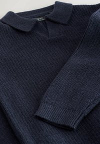 Mørkeblå strikket sweater med krave, der har tekstureret ribning og en afslappet pasform. Materialet fremstår blødt og varmt.