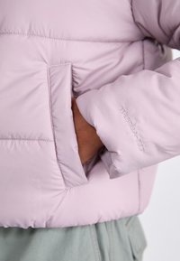 Gaiši rozā pūkaina jaka ar gludu tekstūru, kurai ir sānu kabata un izšūts "THERMAL-FIT" detalizējums uz piedurknes.