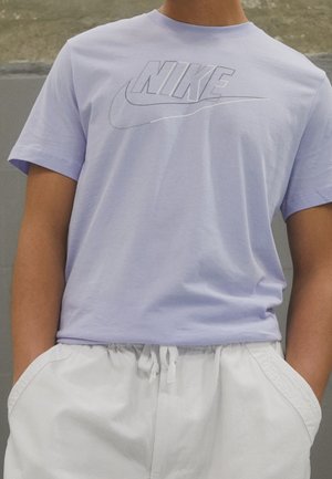 Helles lila Baumwoll-T-Shirt mit einem großen weißen Nike-Logo auf der Vorderseite, kombiniert mit weißen Shorts mit Kordelzug.