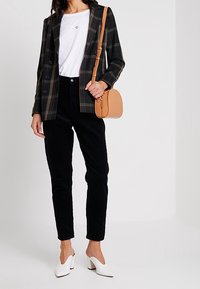 Mustat corduroy-housut, valkoinen t-paita, jossa on pieni sydäntunnus, ruudullinen bleiseri ja beige olkalaukku. Valkoiset korokepohjaiset kengät.