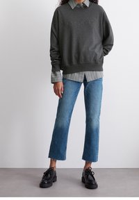 Donkergrijze sweatshirt met reliëf logo "Marc O'Polo", gedragen over een lichtgrijze en witgestreepte blouse. Gepaard met blauwe uitlopende jeans en zwarte schoenen.