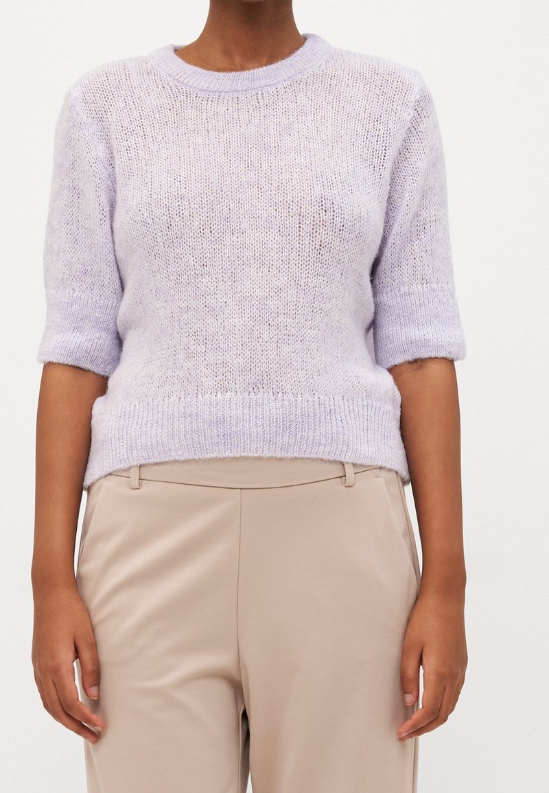 Lila kortärmad stickad tröja med rund halsringning och något ribbad nederkant. Bar över beige byxor som har ett lätt, texturerat tyg.