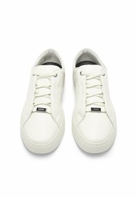 Sneakers bianchi in pelle con superficie testurizzata, caratterizzati da una punta rotonda, chiusura con lacci e un accentuato marchio nero sulla parte anteriore.
