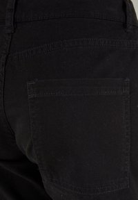 Čierne džinsy z denimu s zadnou vreckom a dvojitým švom, s hladkou textúrou, zachytávajúce detail tkaniny a tvaru.