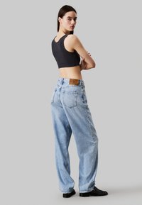 Jeans de tiro alto en azul claro con un corte relajado, diseño minimalista y bolsillos traseros. Combinados con un crop top ajustado en gris oscuro.
