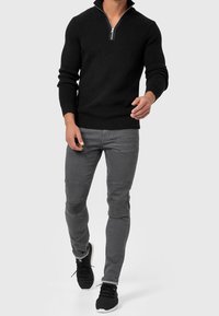 Pull noir à côtes avec un col zippé à quart et des manches longues, associé à un jean gris slim avec des détails de panneaux aux genoux et des accents texturés.