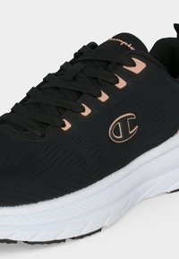 Baskets de sport noires avec semelle blanche, lacets noirs et touches roses, avec le logo Champion sur le côté.
