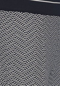 Marineblauw en crèmekleurige stof met een zigzagpatroon. Het materiaal is gebreid, met een textuur oppervlak en een geribde tailleband.