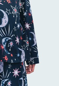 Navy pyjamaset med stjärn- och månmönster i rosa och vitt. Har långa ärmar och mjukt tyg med en avslappnad passform, synligt ärmslut och nederkant.