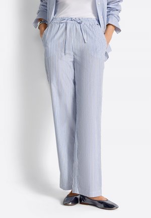 Person trägt hellblau-weiß gestreifte, weit geschnittene Hosen mit Kordelzug in der Taille, kombiniert mit metallisch glänzenden flachen Schuhen.