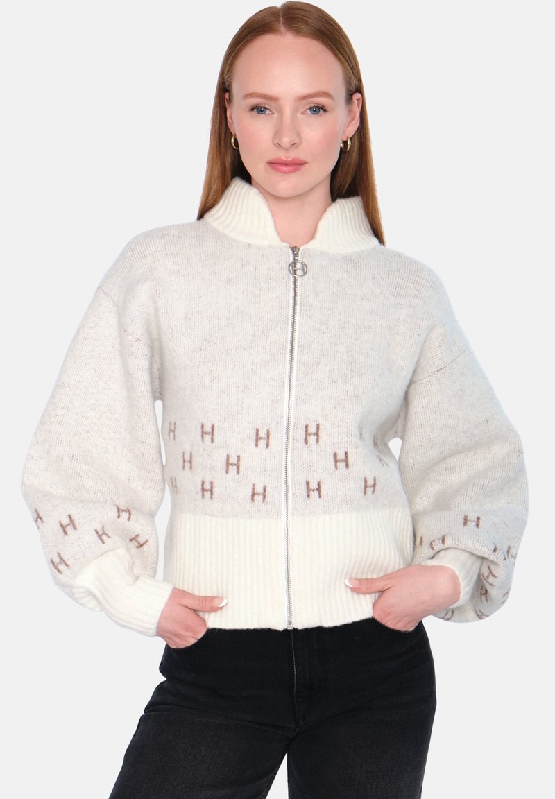 Strikket jakke med glidelås i kremfarge med ribbet kant og mansjetter. Har mønstrede detaljer med bokstavene "H" i lysbrun. Koselig og strukturert design.
