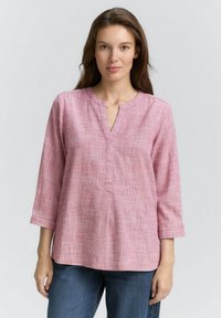 Haut à manches longues à carreaux roses avec un décolleté en V. Tissu léger, coupe décontractée, avec une couture centrale et des poignets retroussés. Associé à un jean bleu.