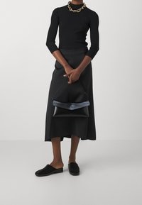 Top de cuello alto de canalé negro, falda midi plisada negra y bolso de cuero negro. Lleva mules negros y un collar de cadena dorada como acento.