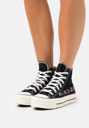 Schwarze High-Top-Sneaker aus Canvas, mit weißen Schnürsenkeln, einer strukturierten Gummisohle und bunten gestickten Designs an den Seiten.