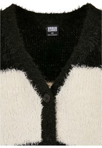 Cardigan en maille floue noir et blanc avec encolure en V, un bouton noir unique et étiquette Urban Classics XS à l'intérieur du col.