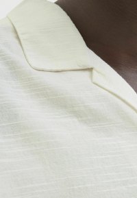 Collared blouse in light cream, featuring a textured fabric with subtle horizontal stripes and a soft, relaxed neckline.