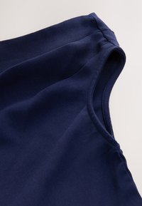 Navy blue sleeveless top made from smooth, lightweight fabric. Features a rounded neckline and gently curved armholes.