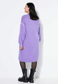 Abito maglione viola con maniche lunghe, orlo a coste e dettagli in bianco sulle spalle. Indossato con stivali neri al ginocchio.