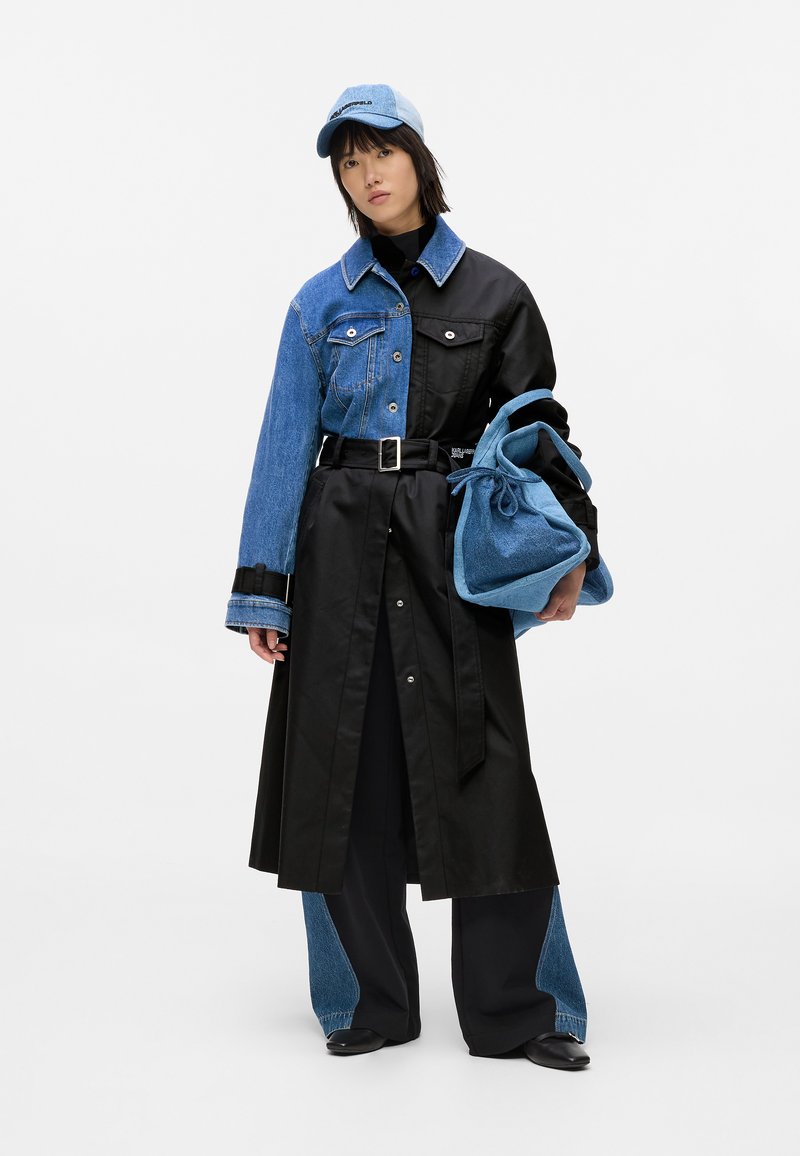 Jeansowa i czarna tkaninowa kurtka z pasem w talii, długimi rękawami oraz mieszanką tekstur. Pasująca niebieska czapka i niebieska torba na sznurku.