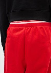 Czerwone dresy z elastycznym pasem, z białymi i czerwonymi pasami, zestawione z czarną bluzą. Miękka bawełniana tkanina, luźny krój.