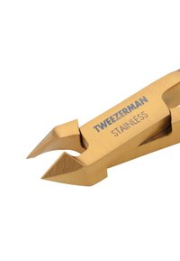 Obcinacz do paznokci Tweezerman ze stali nierdzewnej o złotym odcieniu, z ostrymi, nachylonymi krawędziami tnącymi na białym tle.