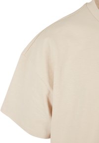 T-shirt en coton beige, coupe décontractée, manches courtes et col rond. Texture douce avec des ourlets cousus.