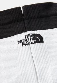Calcetines en blanco y negro con una textura acanalada y un destacado logotipo negro de "The North Face" en una banda blanca.