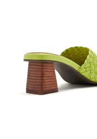 Sandale à glissière tressée verte avec un talon en bois carré. La bride présente un design texturé et tressé, complétant la semelle lisse.
