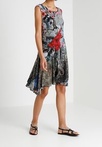 Hihaton kukkakuosinen mekko useissa väreissä, mukaan lukien punainen, musta ja sininen. Mekossa on liehuva helma ja sekoitettuja kangaspintoja. Yhdistetty mustien sandaalien kanssa.