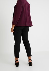 Pruimenblazer met een gestructureerde afwerking, gecombineerd met zwarte slim-fit broek en zwarte enkelsandalen met bandje. Voorzien van een drieknoopaccent op de mouw.