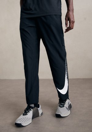 Pantalons de sport noirs avec un logo Nike blanc et un motif texturé. Fabriqués à partir d'un matériau léger et respirant, avec un design fuselé.