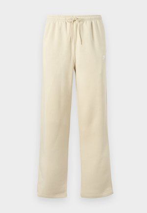 Pantalones deportivos beige de corte holgado con cintura elástica y cordón ajustable, con un pequeño logo blanco de Nike en el muslo izquierdo.