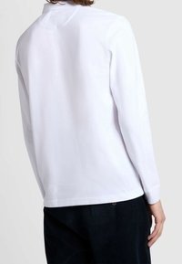 Chemise blanche à manches longues avec un col classique, une texture lisse et un ourlet droit. Le dos présente un détail discret de renfort et des coutures minimales.