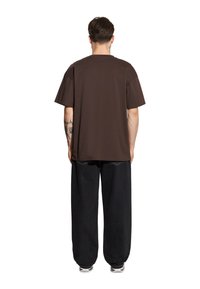 Brązowa koszulka z krótkim rękawem o luźnym kroju, w połączeniu z luźnymi czarnymi dżinsami. Gładki design, miękka tekstura i neutralne kolory.