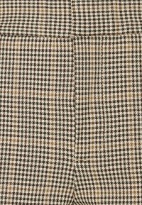 Brun och beige tyg med hundtandsmönster, med en slät textur och skräddarsydd design med synliga plisseringar.